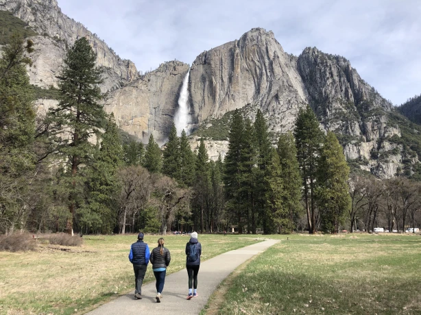 Drei Menschen wandern durch Yosemite Tal mit Berg und Wasserfall im Hintergrund