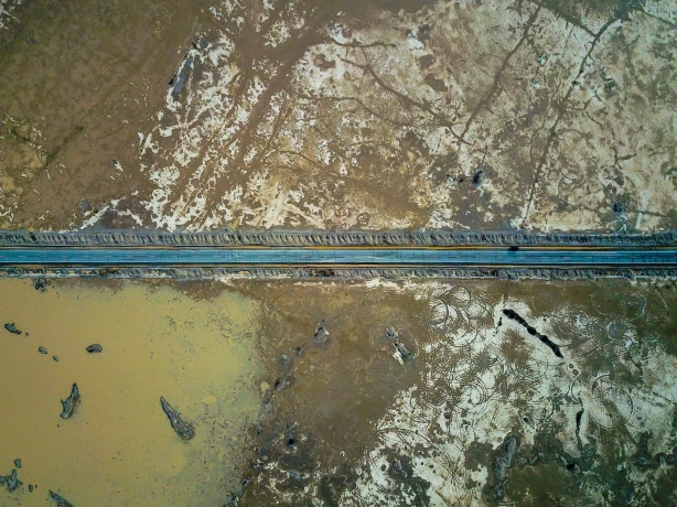 Eine gerade Straße, die durch die kargen Wüstenebenen des Death Valley führt, von oben gesehen, mit Wasserflecken und strukturierter, rissiger Erde auf beiden Seiten.