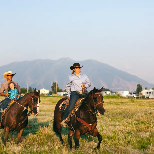Twee mensen met een kind en een cowboyhoed rijden op twee paarden in een veld