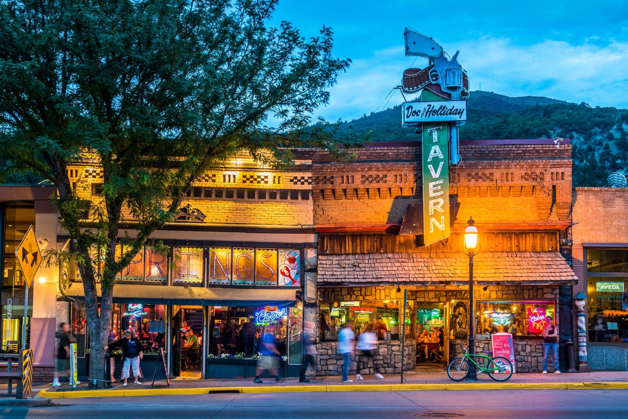 Abendstimmung in der historischen Innenstadt von Glenwood Springs, Colorado. Die beleuchtete Doc Holliday Tavern und umliegende Bars verleihen der Straße mit ihren Westernfassaden eine lebendige Atmosphäre.