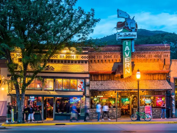 Abendstimmung in der historischen Innenstadt von Glenwood Springs, Colorado. Die beleuchtete Doc Holliday Tavern und umliegende Bars verleihen der Straße mit ihren Westernfassaden eine lebendige Atmosphäre.