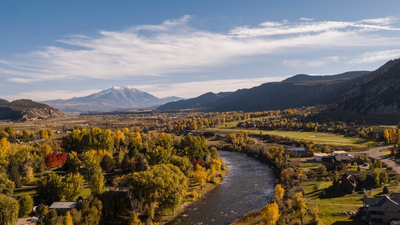 Blick über Glenwood Springs in Colorado mit dem Colorado River, herbstlich gefärbten Bäumen und dem schneebedeckten Mount Sopris im Hintergrund.