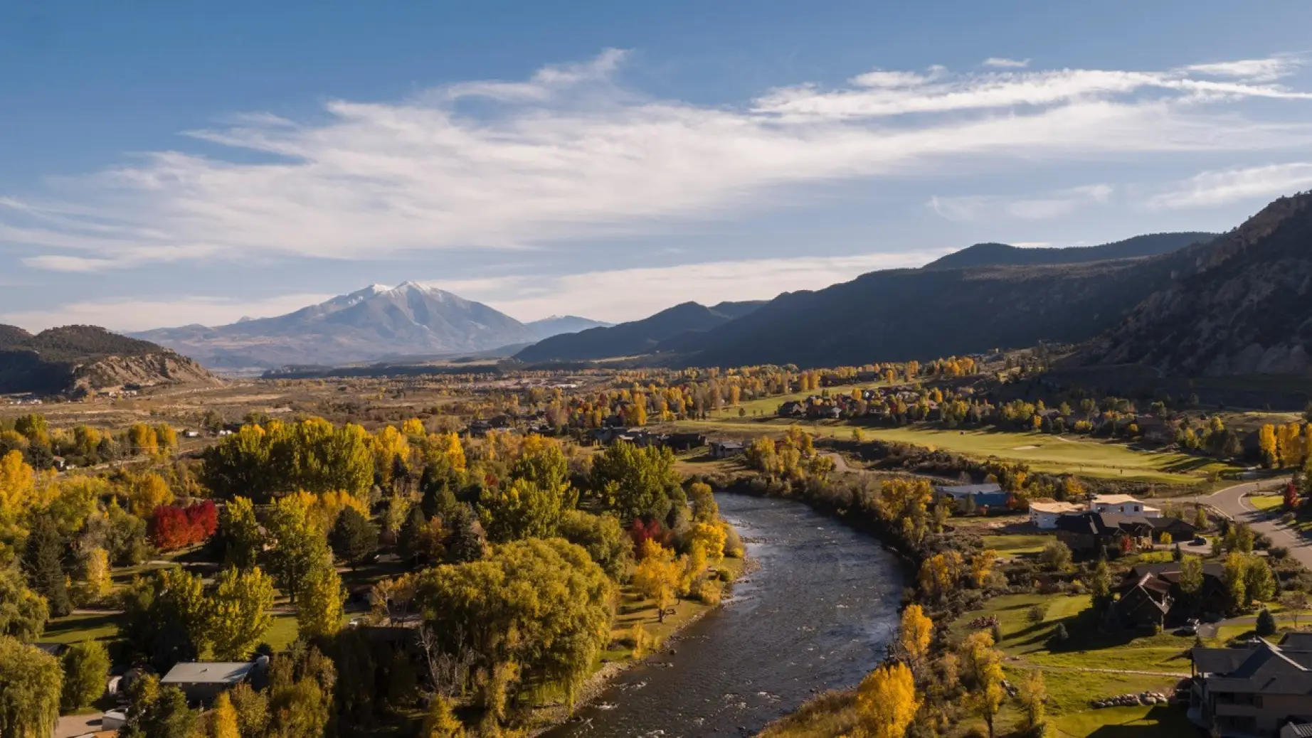 Blick über Glenwood Springs in Colorado mit dem Colorado River, herbstlich gefärbten Bäumen und dem schneebedeckten Mount Sopris im Hintergrund.