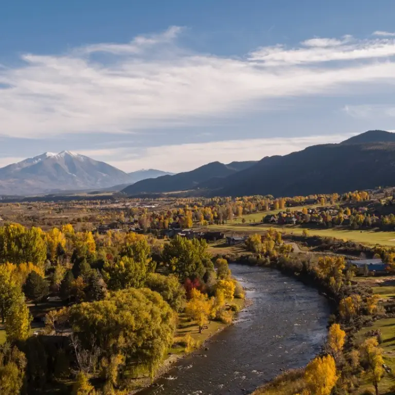 Blick über Glenwood Springs in Colorado mit dem Colorado River, herbstlich gefärbten Bäumen und dem schneebedeckten Mount Sopris im Hintergrund.