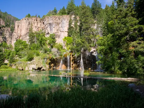 Hanging Lake bei Glenwood Springs in Colorado mit türkisfarbenem Wasser, kleinen Wasserfällen und steilen Felswänden, umgeben von dichtem Wald.