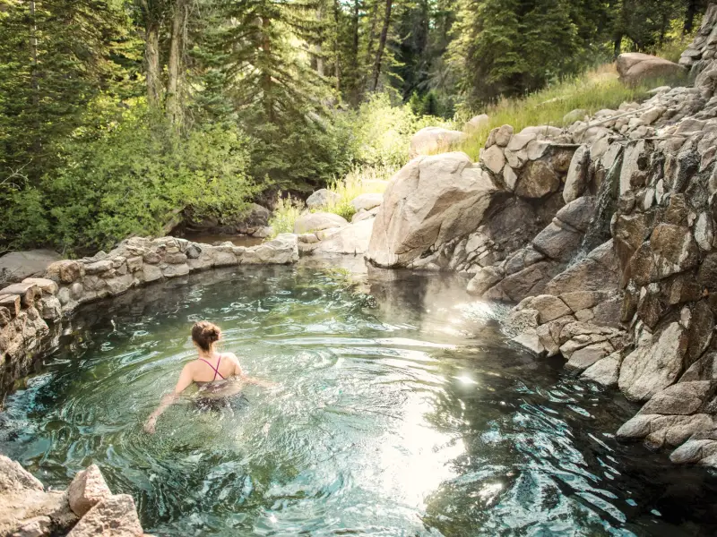 Eine Frau entspannt sich in einer natürlichen heißen Quelle in den Bergen von Colorado. Das von Felsen umgebene Thermalbecken liegt mitten in einem Wald.