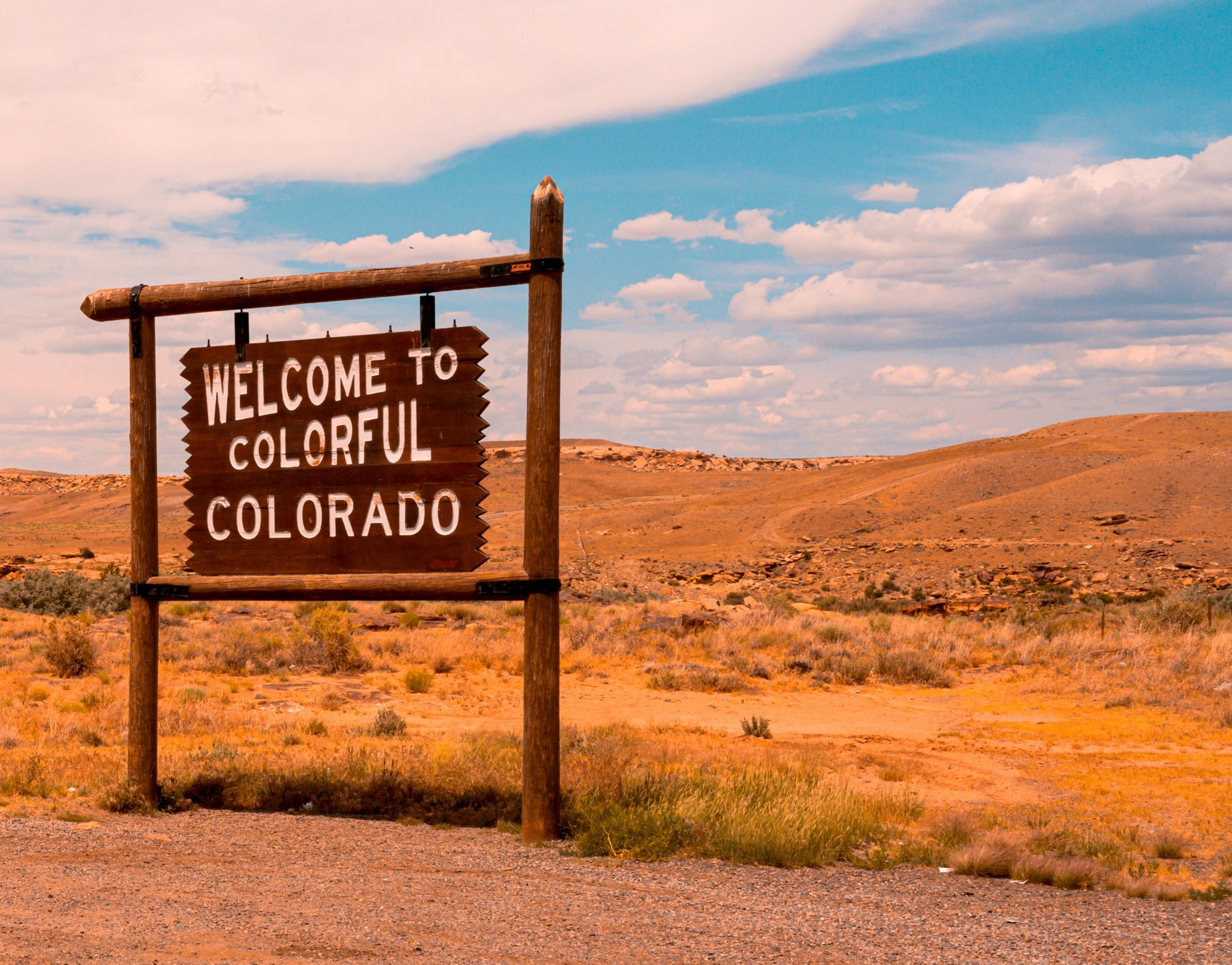 Holzschild mit der Aufschrift "Welcome to colorful Colorado" am Straßenrand einer prärieartigen Landschaft