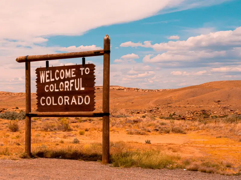 Holzschild mit der Aufschrift "Welcome to colorful Colorado" am Straßenrand einer prärieartigen Landschaft
