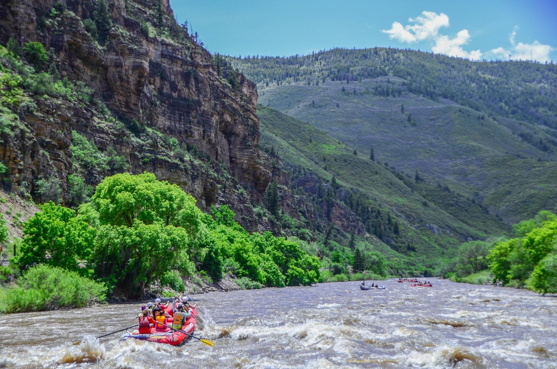 Mehrere Schlauchboote fahren beim Wildwasser-Rafting auf dem Colorado River durch eine von steilen Felswänden und grünen Berghängen geprägte Landschaft bei Glenwood Springs in Colorado.