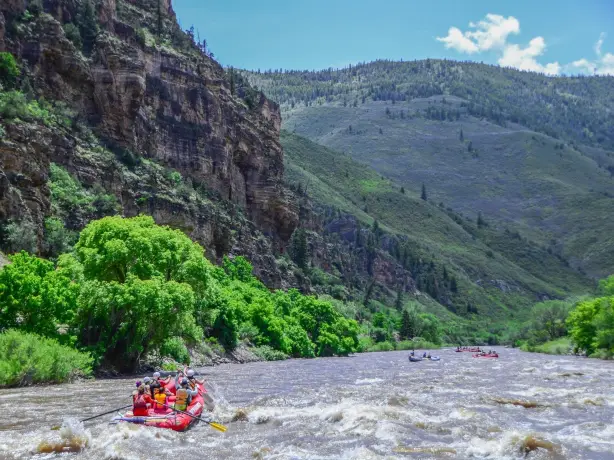 Mehrere Schlauchboote fahren beim Wildwasser-Rafting auf dem Colorado River durch eine von steilen Felswänden und grünen Berghängen geprägte Landschaft bei Glenwood Springs in Colorado.