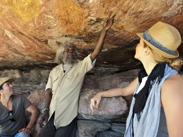 A local Aboriginal guide showing a pair of tourists ancient rock art in Australia