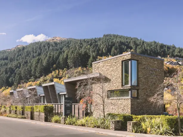 Ein modernes, mit Stein verkleidetes Boutique-Hotel mit kantigen Dachlinien, umgeben von herbstlichem Laub und mit Kiefern bewachsenen Hügeln in Queenstown, Neuseeland