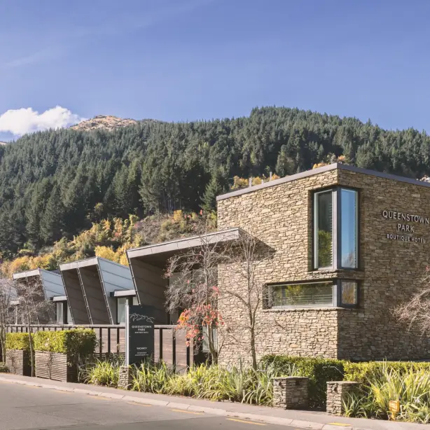 Contemporary stone-clad boutique hotel with angular rooflines surrounded by autumn foliage and pine-covered hills in Queenstown, New Zealand
