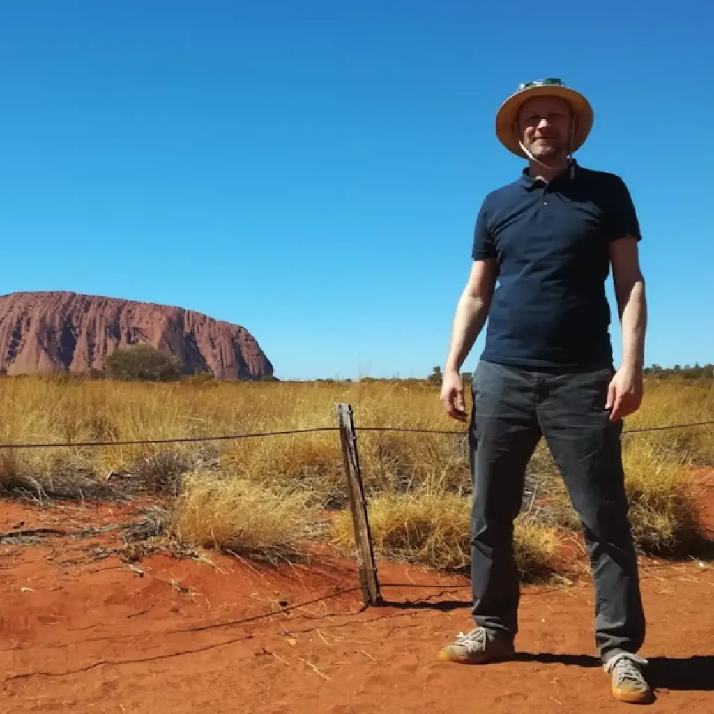 Mann steht auf rotem Sand vor dem Uluru in Australien