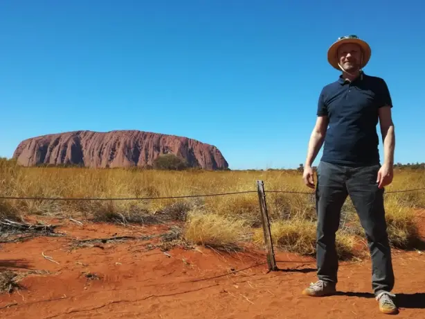 Mann steht auf rotem Sand vor dem Uluru in Australien