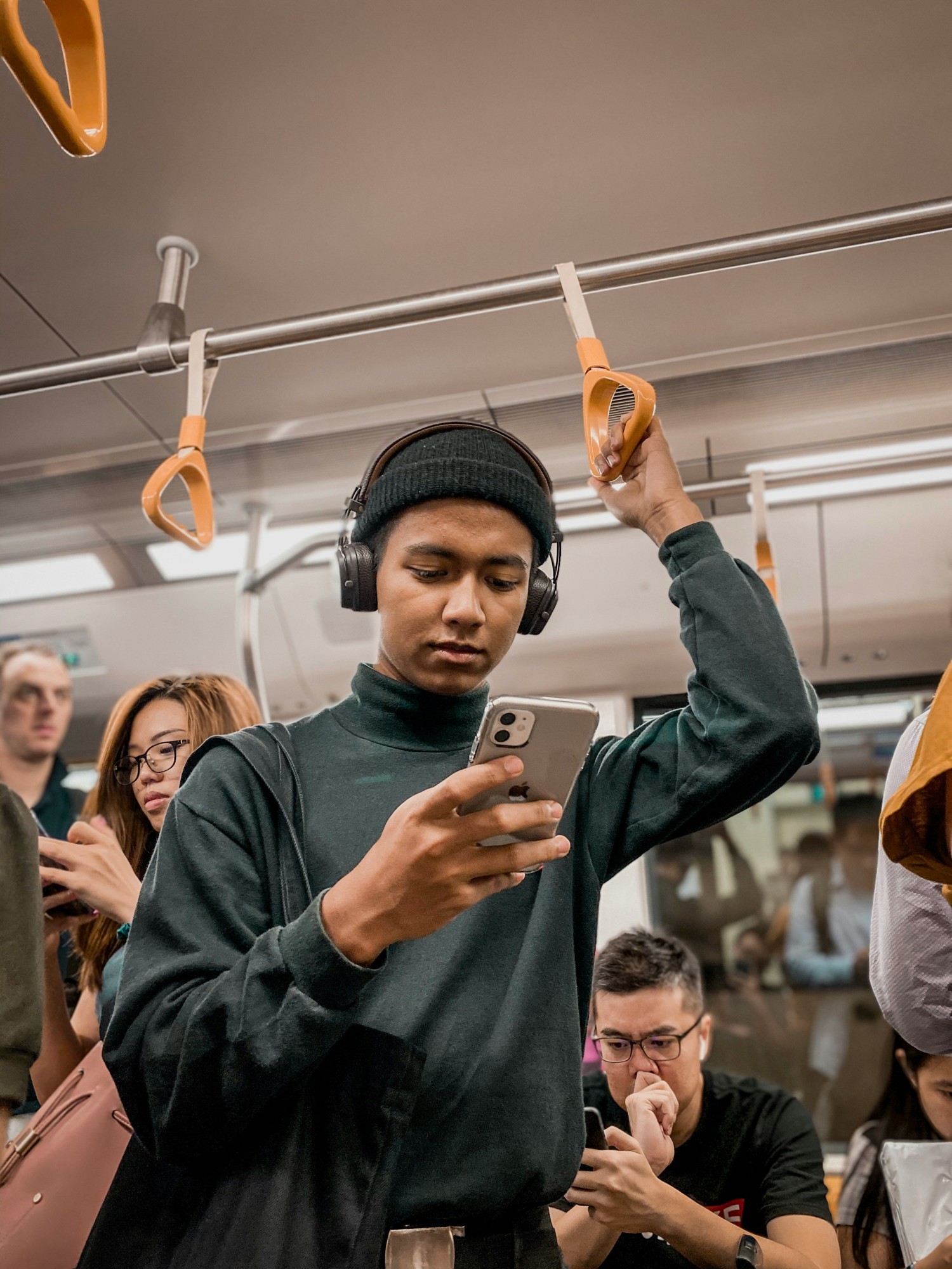 Ein Mann fährt im Zug, während er auf sein Handy schaut und Kopfhörer trägt
