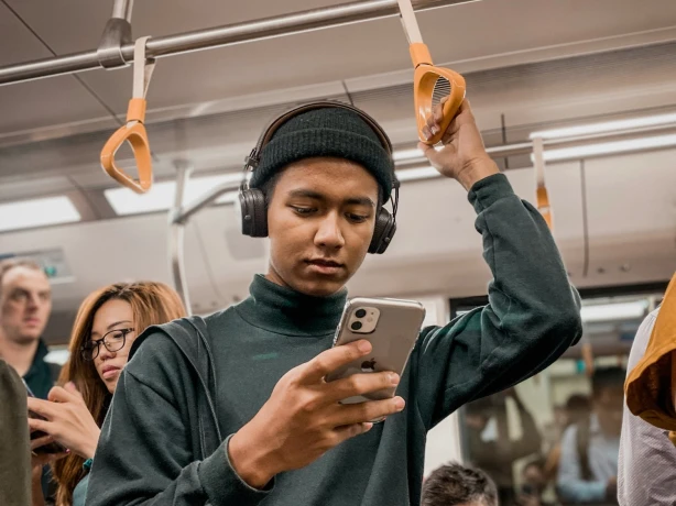 Ein Mann fährt im Zug, während er auf sein Handy schaut und Kopfhörer trägt