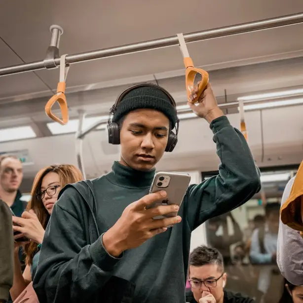 Een man zit in de trein terwijl hij op zijn mobiele telefoon kijkt en een koptelefoon draagt