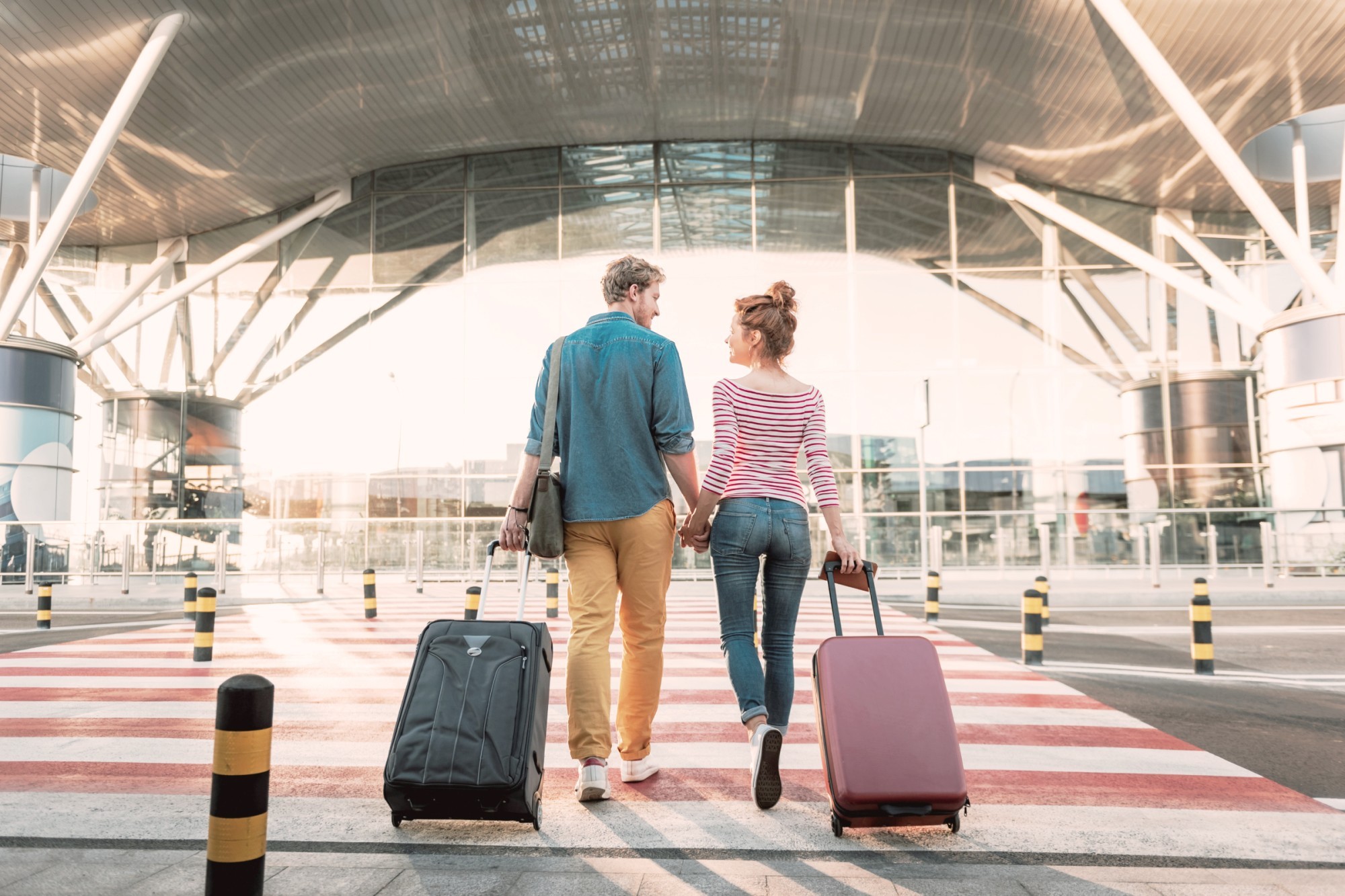 Ein Pärchen mit Ziehkoffern hält Händchen und läuft in Flughafen