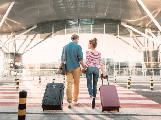 Ein Pärchen mit Ziehkoffern hält Händchen und läuft in Flughafen