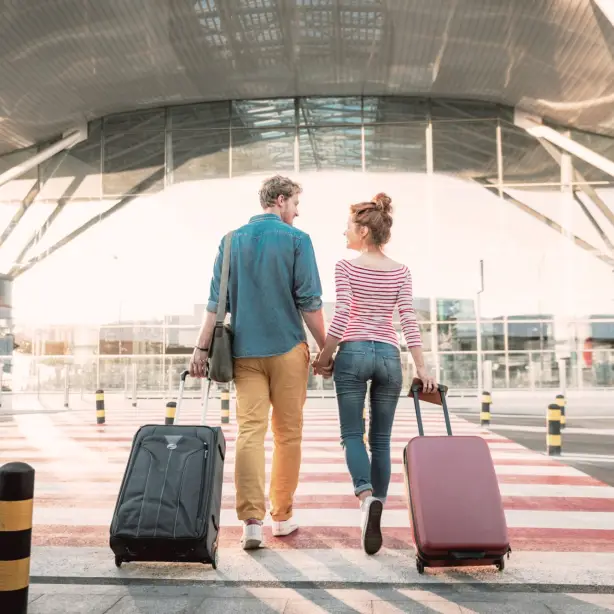 Ein Pärchen mit Ziehkoffern hält Händchen und läuft in Flughafen