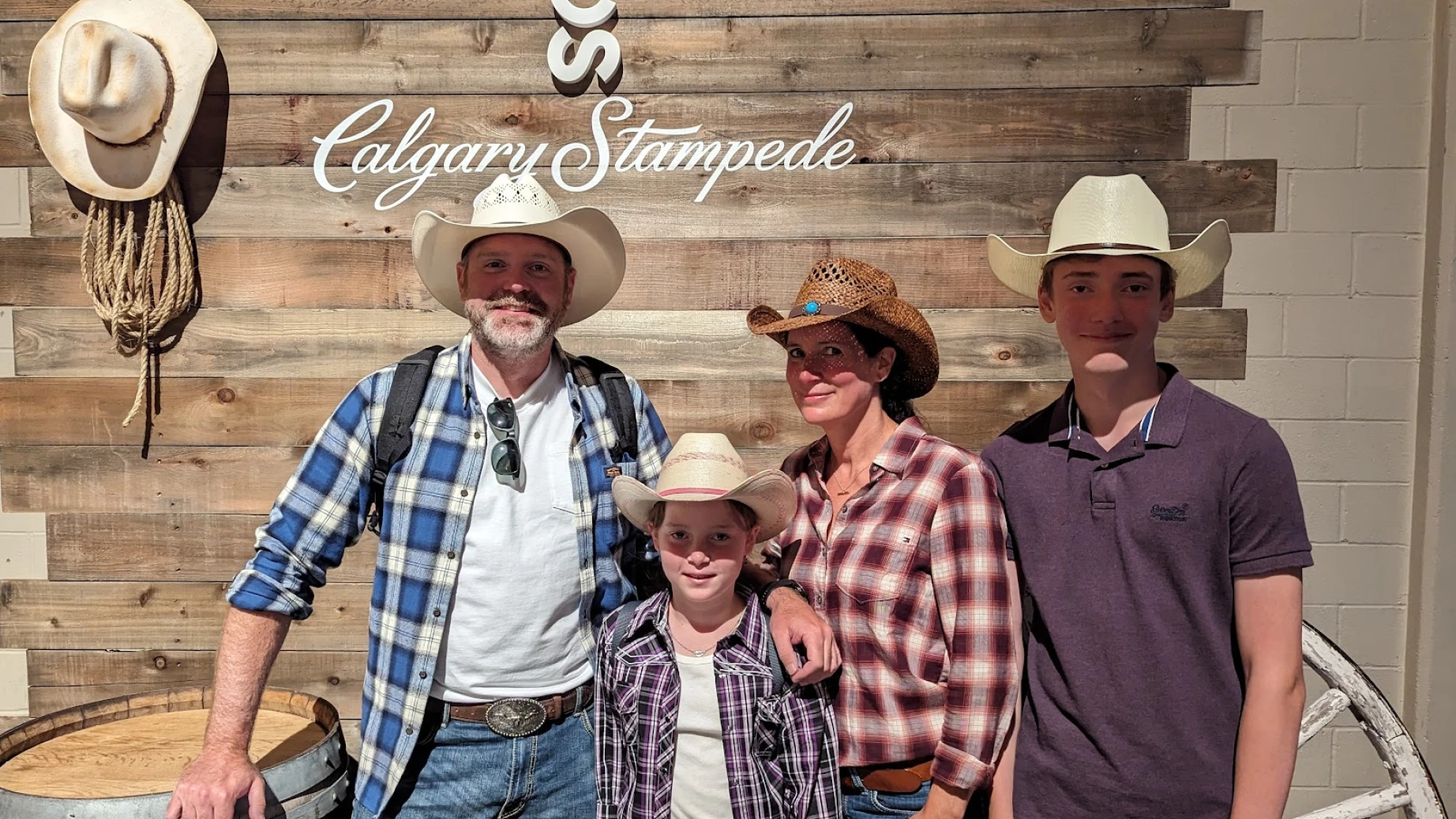 Familie mit zwei Kindern trägt Cowboyhüte und posiert vor Holzwand auf der Calgary Stampede
