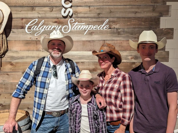 Familie mit zwei Kindern trägt Cowboyhüte und posiert vor Holzwand auf der Calgary Stampede