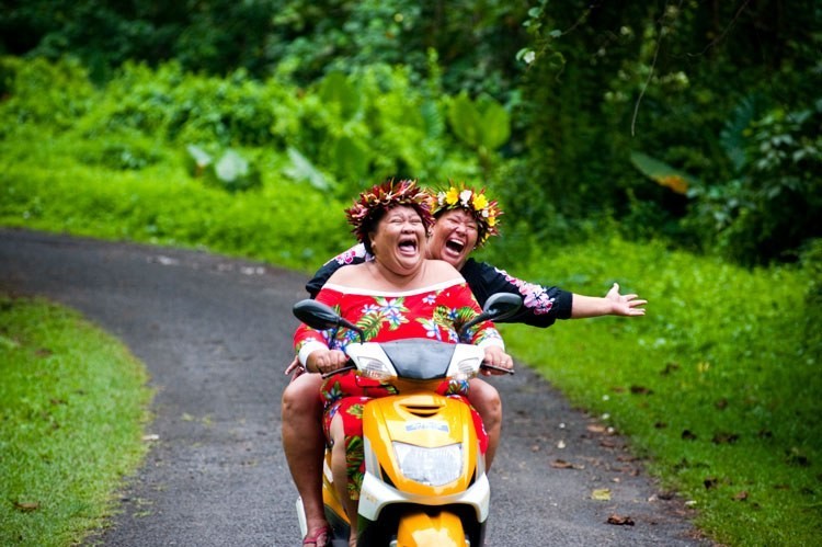 Two Cook Islanders laugh while riding a scooter through the forest