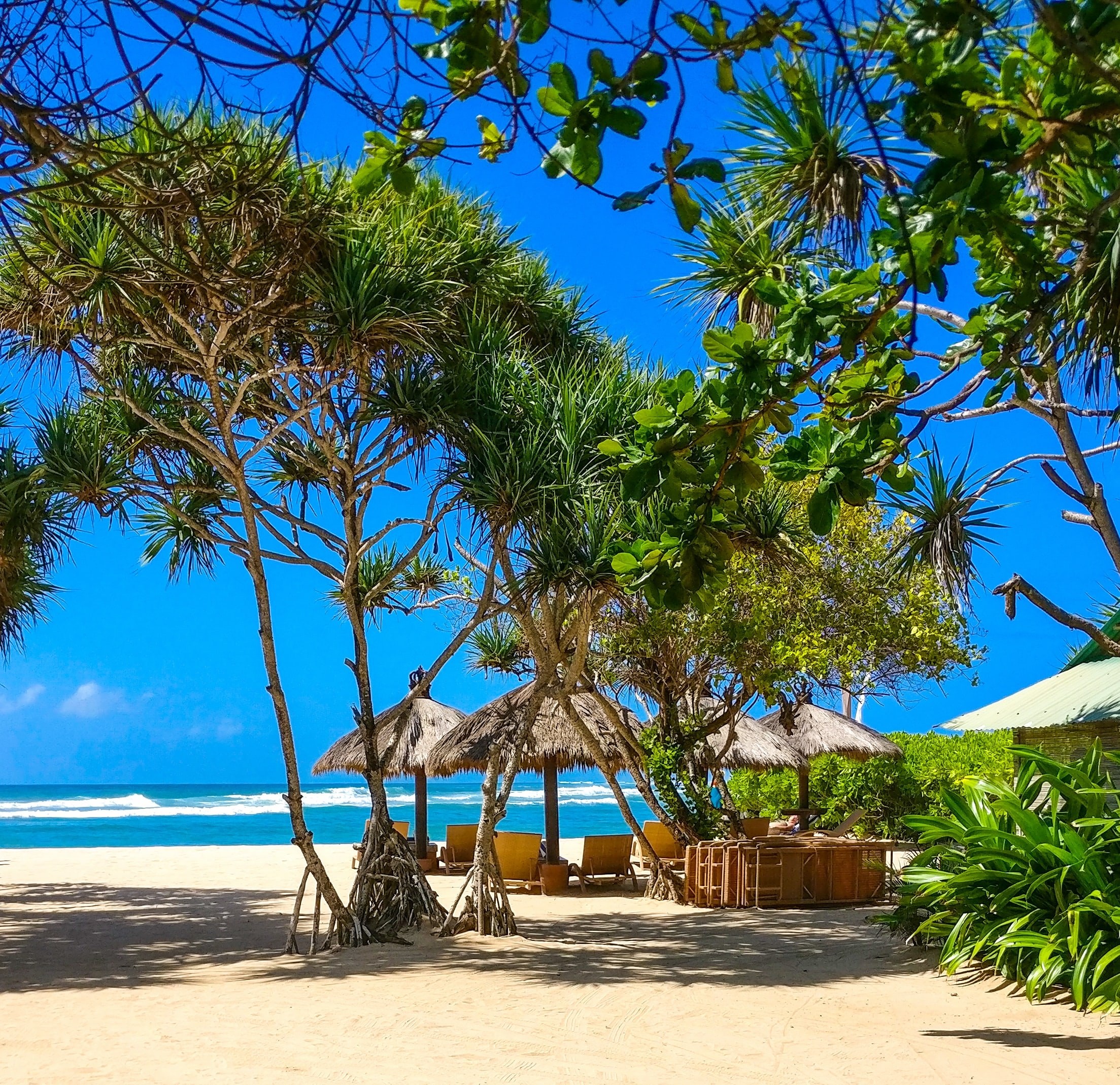 Strand mit Strohhütten und Sitzgelegenheiten mit Blick auf den Ozean in Bali