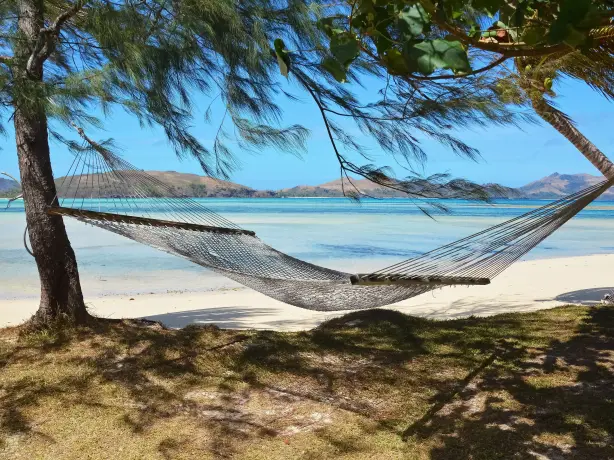 A hammock tied between two trees on the beach with the ocean and other islands in the background