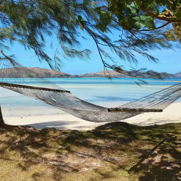 Een hangmat tussen twee bomen op het strand met de oceaan en andere eilanden op de achtergrond