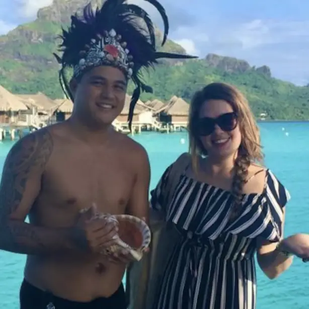Sylvie en een Maori-man lachen naar de camera met de oceaan en bergen op de achtergrond