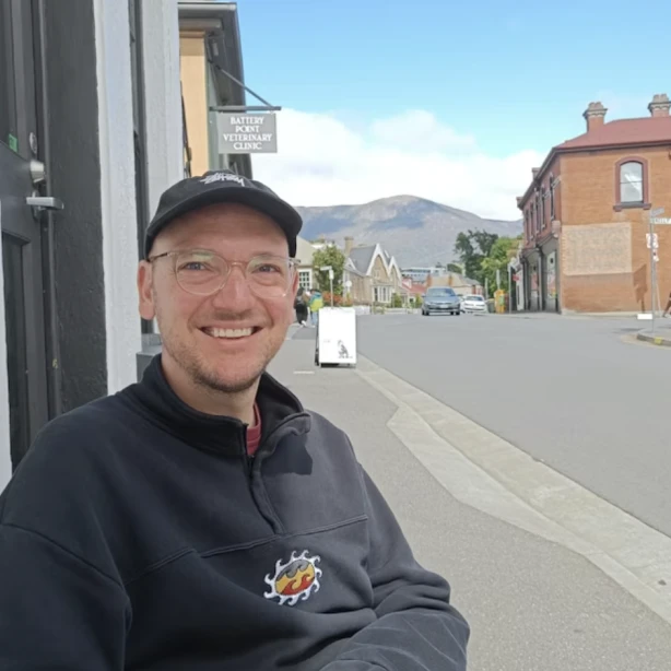 Sjoerd lacht naar de camera met een stad en bergen op de achtergrond
