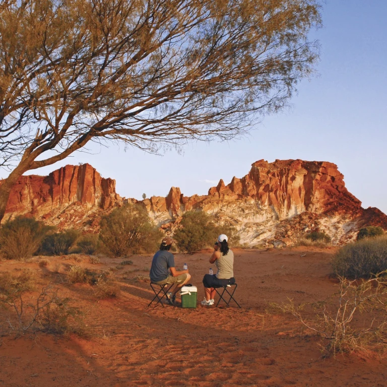 Paar zittend op klapstoeltjes in de Australische outback voor rode rotsen