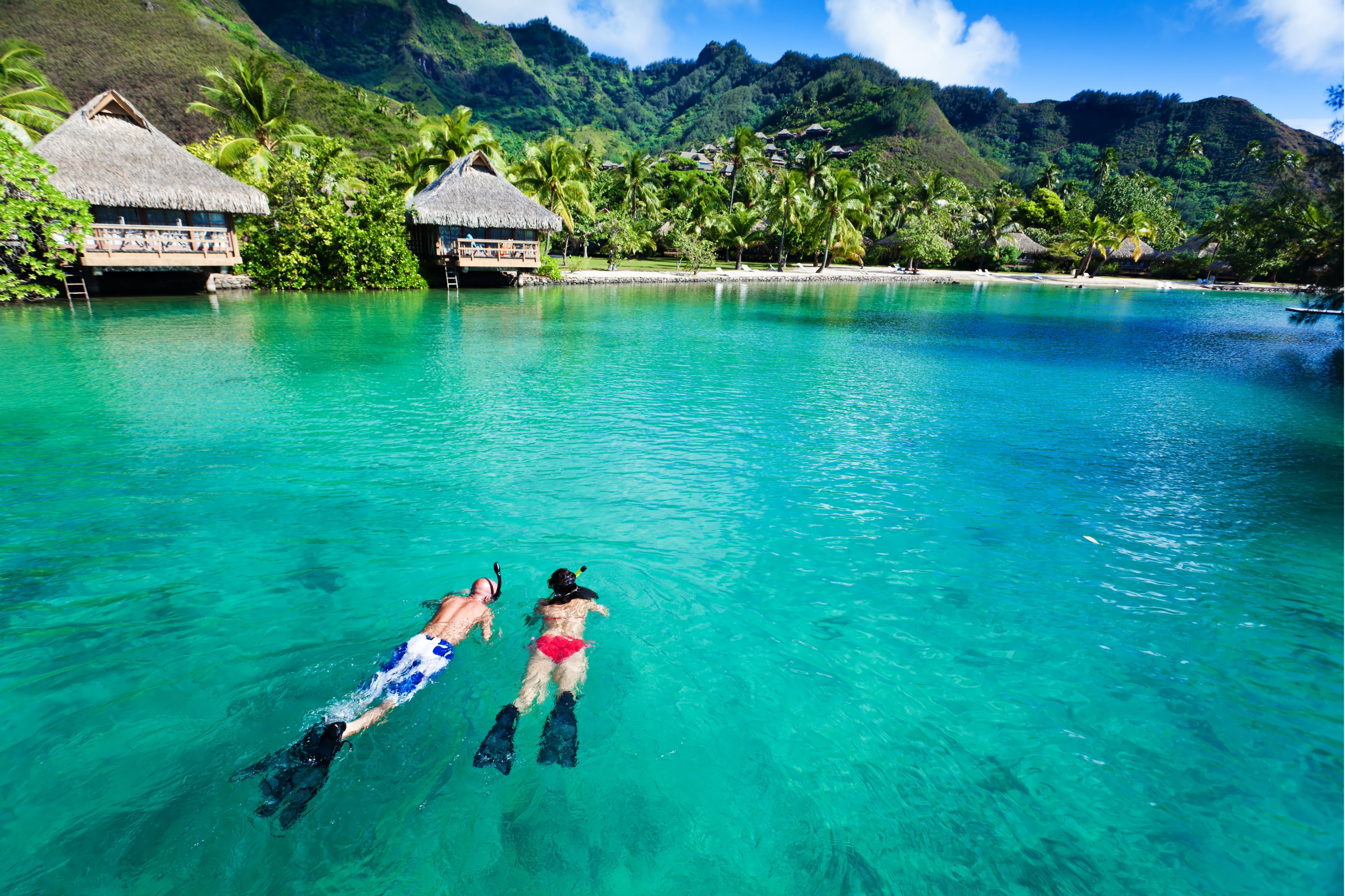 Twee mensen snorkelen in het turquoise water van Tahiti met waterhutten en bergen op de achtergrond