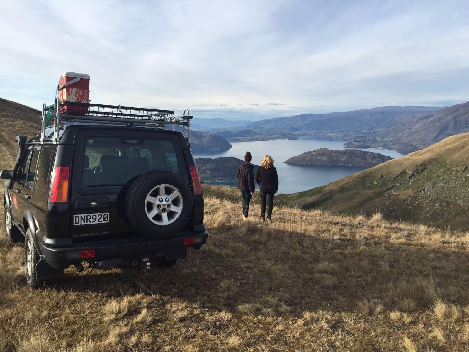 Twee mensen staan naast een 4x4 voertuig en kijken uit over een meer in Queenstown, Nieuw-Zeeland