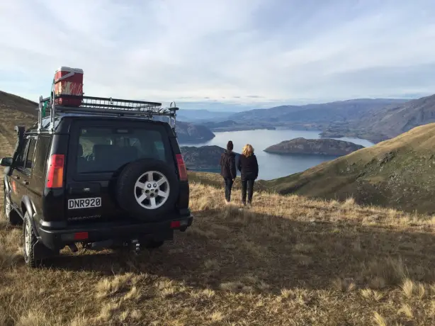 Zwei Menschen stehen neben einem Geländewagen und blicken auf einen See in Queenstown, Neuseeland
