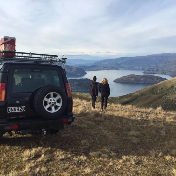 Twee mensen staan naast een 4x4 voertuig en kijken uit over een meer in Queenstown, Nieuw-Zeeland