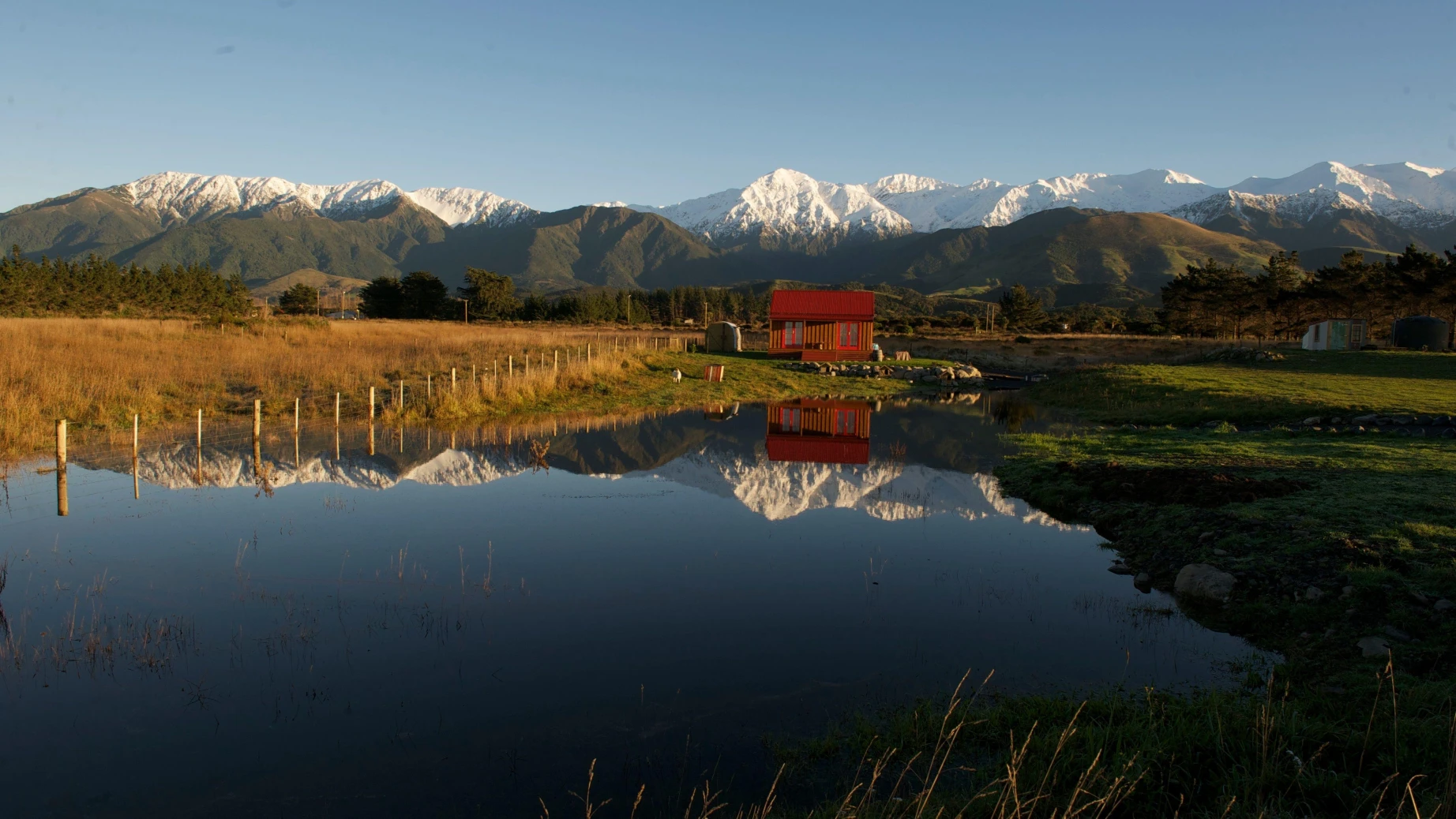 A small accommodation with snow-covered mountains in the background reflected in the water, Kaikoura New Zealand