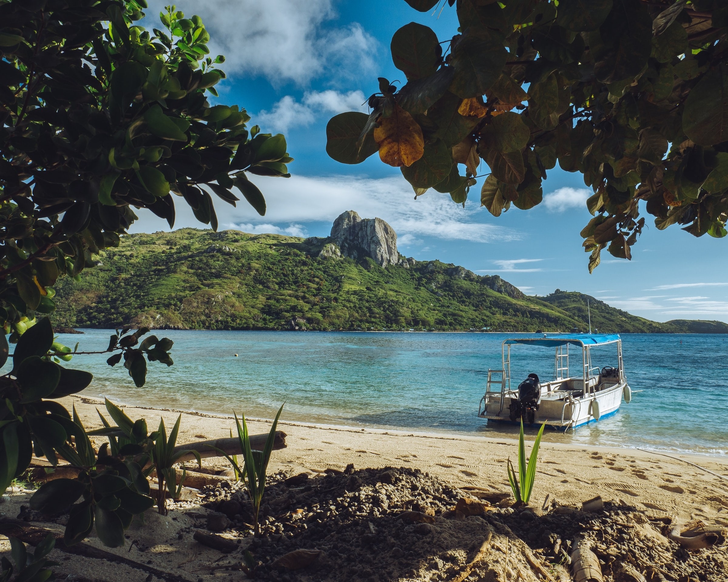 Fiji beach with boat in the water and mountains in the background