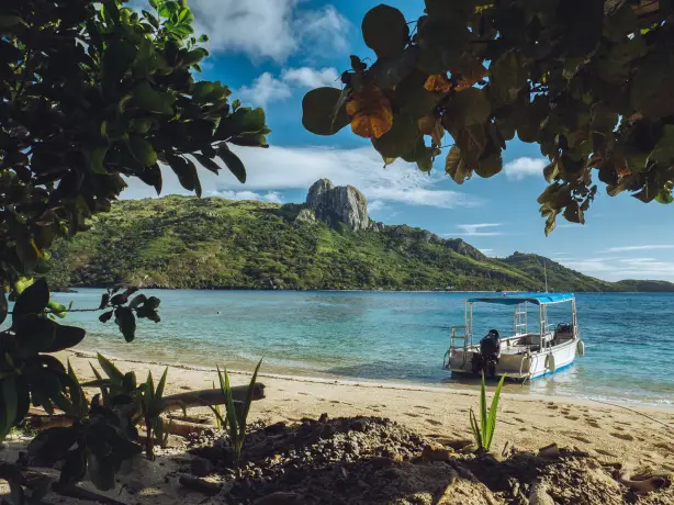 Fiji beach with boat in the water and mountains in the background