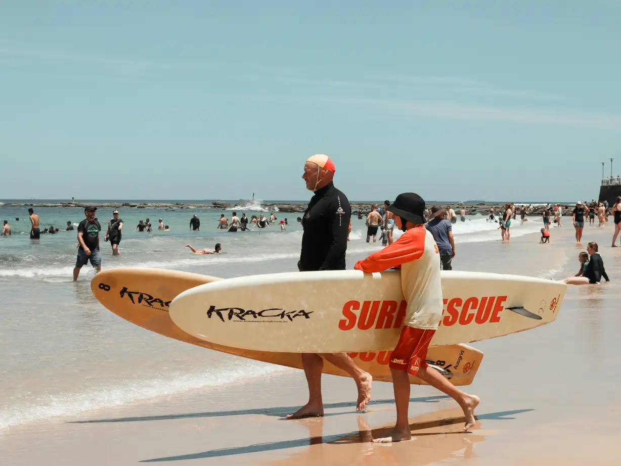 AU NSW Newcastle surfers lopen op het strand