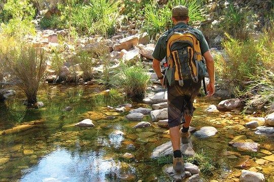 Wanderer mit großem Rucksack läuft während einer Wandertour über Steine im Wasser