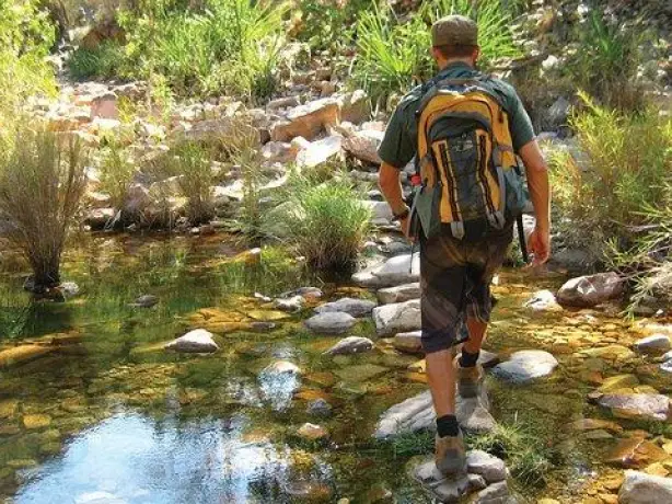 Wanderer mit großem Rucksack läuft während einer Wandertour über Steine im Wasser