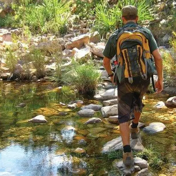 Wanderer mit großem Rucksack läuft während einer Wandertour über Steine im Wasser