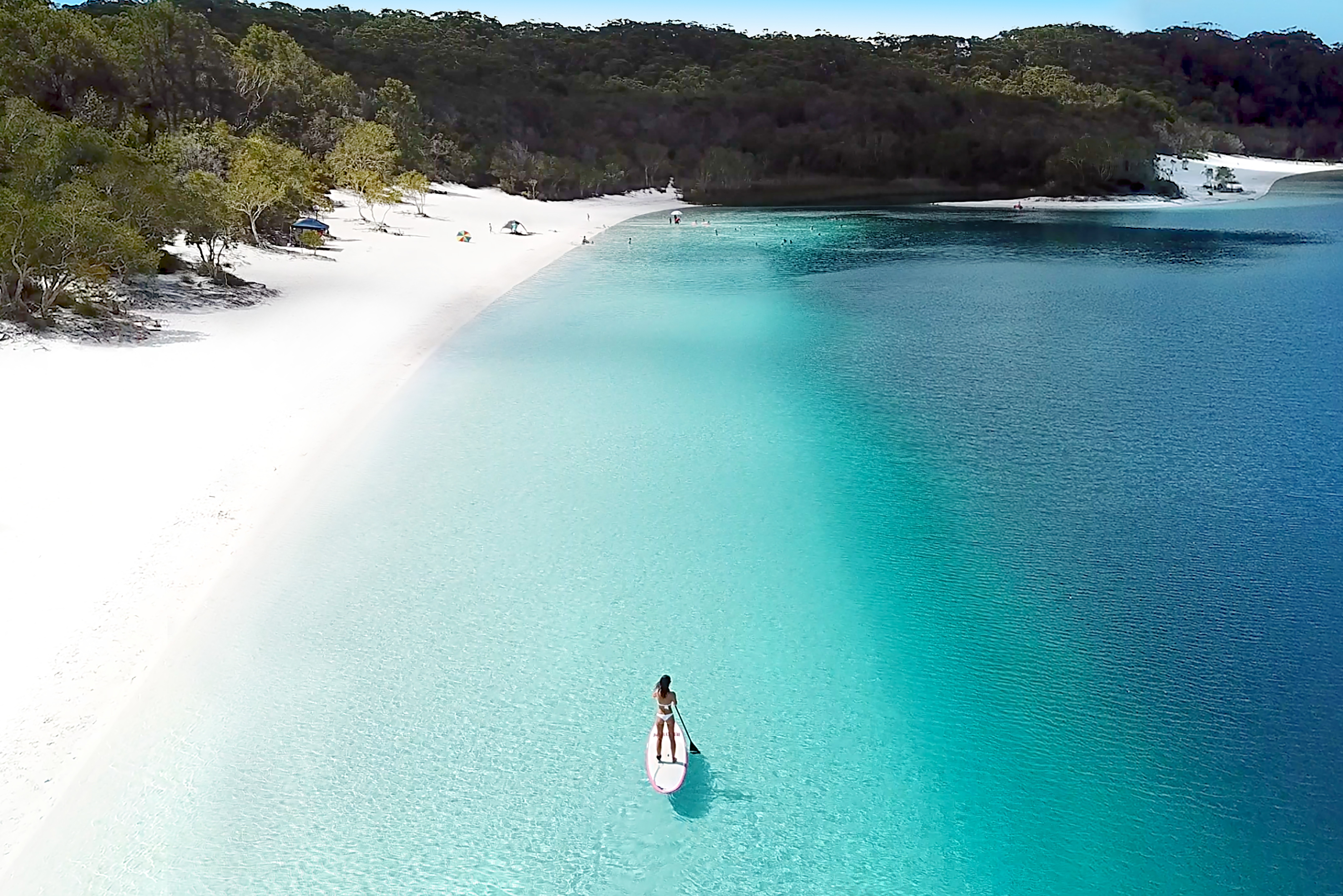 Ein Paddleboarder paddelt entlang eines weißen Sandstrandes auf K'Gari / Fraser Island, Queensland.