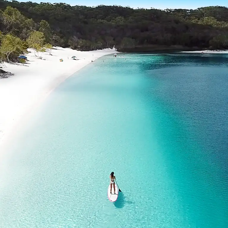 A paddleboarder paddles along a white sand beach on K'Gari / Fraser Island, Queensland