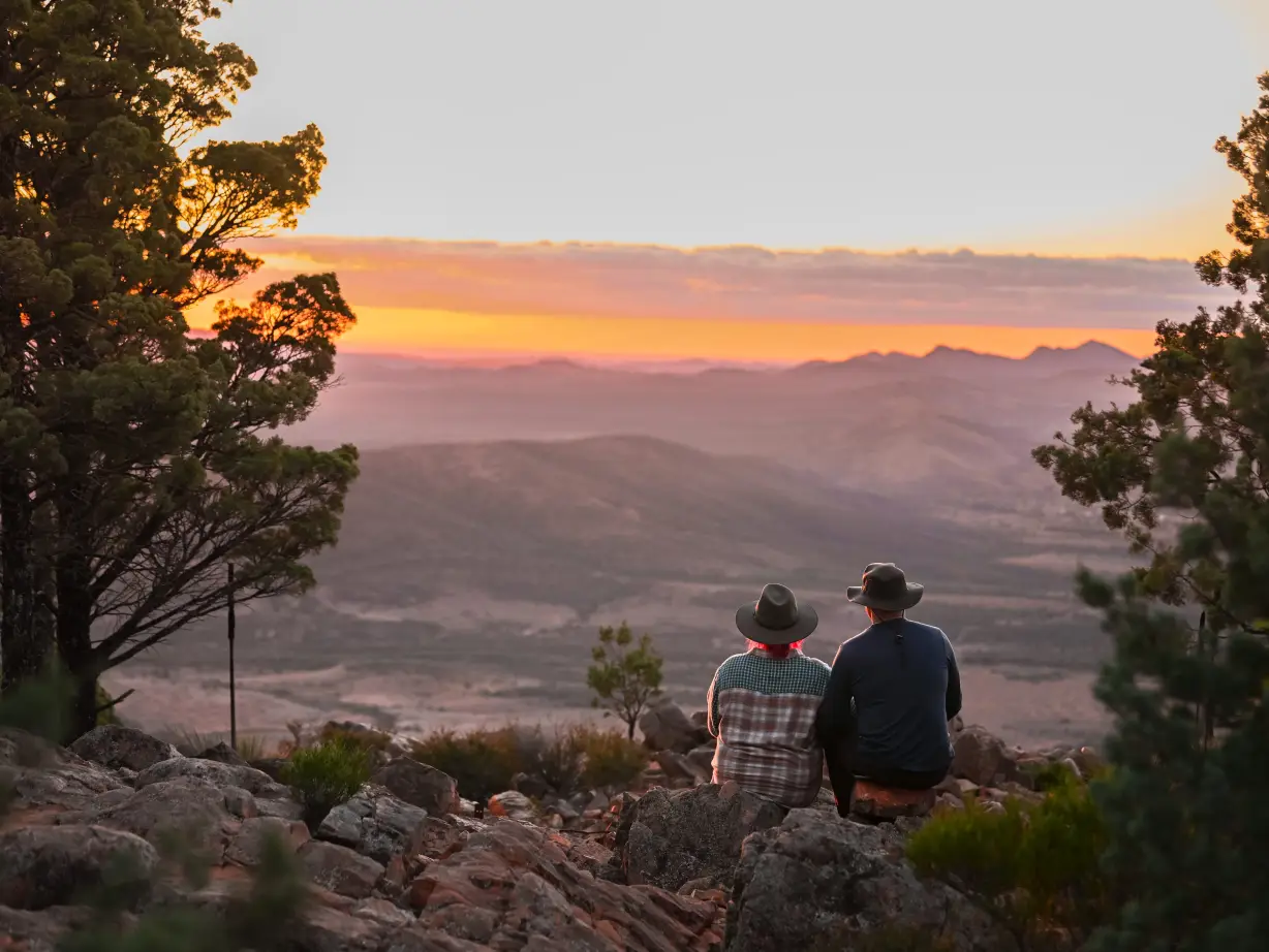 Ein Paar sitzt zusammen und blickt bei Sonnenuntergang über die Berge in den Flinders Ranges im Outback, Australien