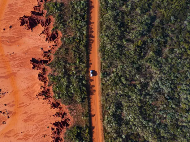 Ein Auto fährt auf einer roten Schotterstraße in Broome, Westaustralien
