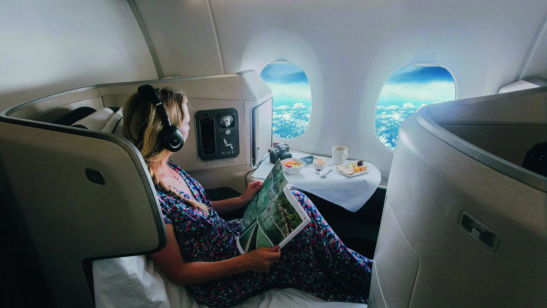 Eine Frau mit Kopfhörern liest eine Zeitschrift im Flugzeug in der Business Class